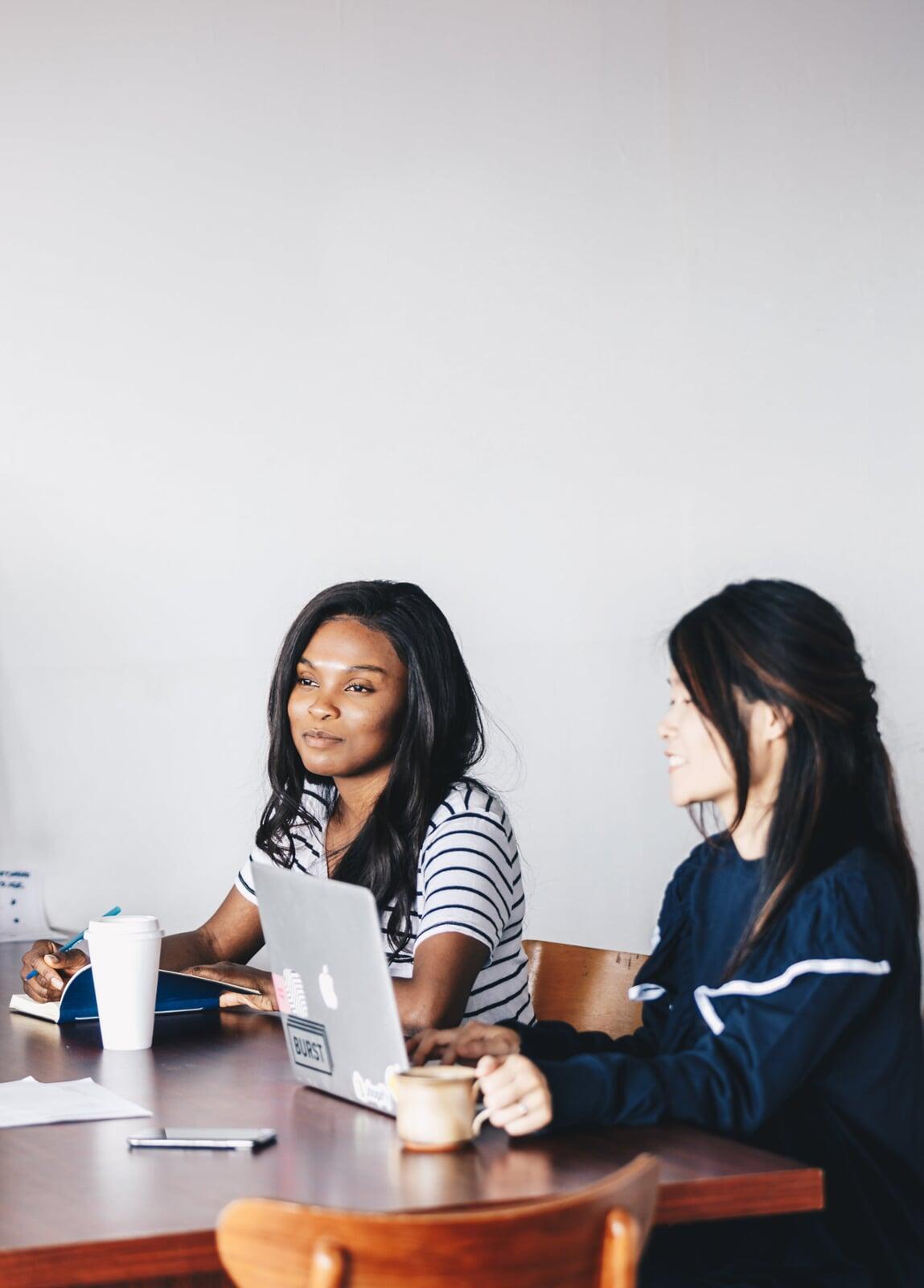Two women share desk space as they spend time working away on their laptops